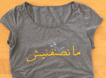 zu sehen ist ein graues T-Shirt mit gelber arabischer Schrift.